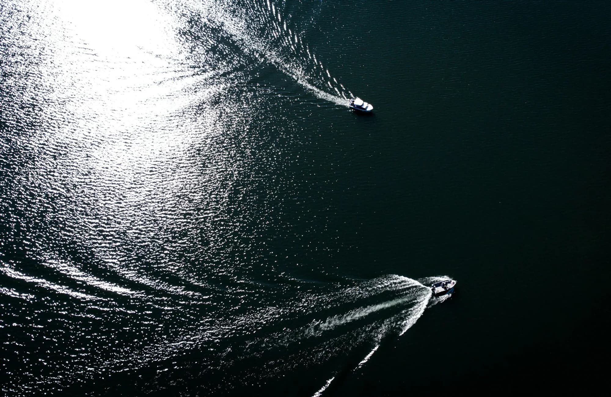 Two boats crossing dark blue water from an aerial viewpoint.