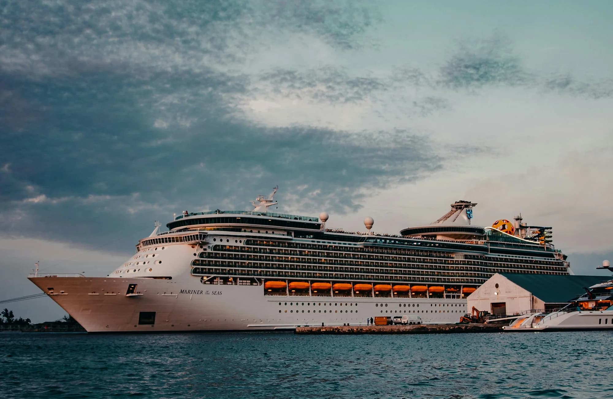 A cruise ship moving across open water beneath scattered clouds.